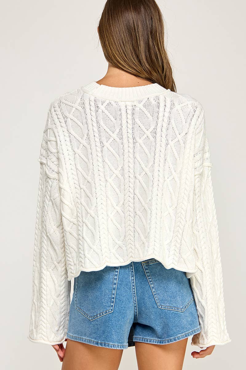 A woman shown from the back wearing a white cable-knit cropped sweater and blue denim shorts against a plain light background.