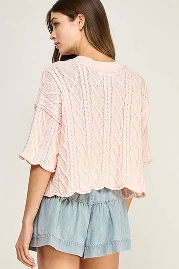 Woman wearing a pink cable knit top and denim shorts on a plain background