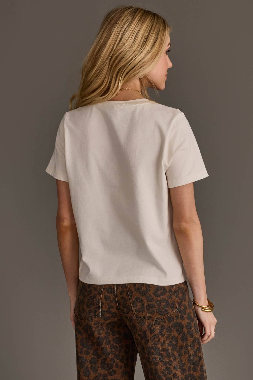 Woman wearing a beige t-shirt and leopard print pants against a gray background