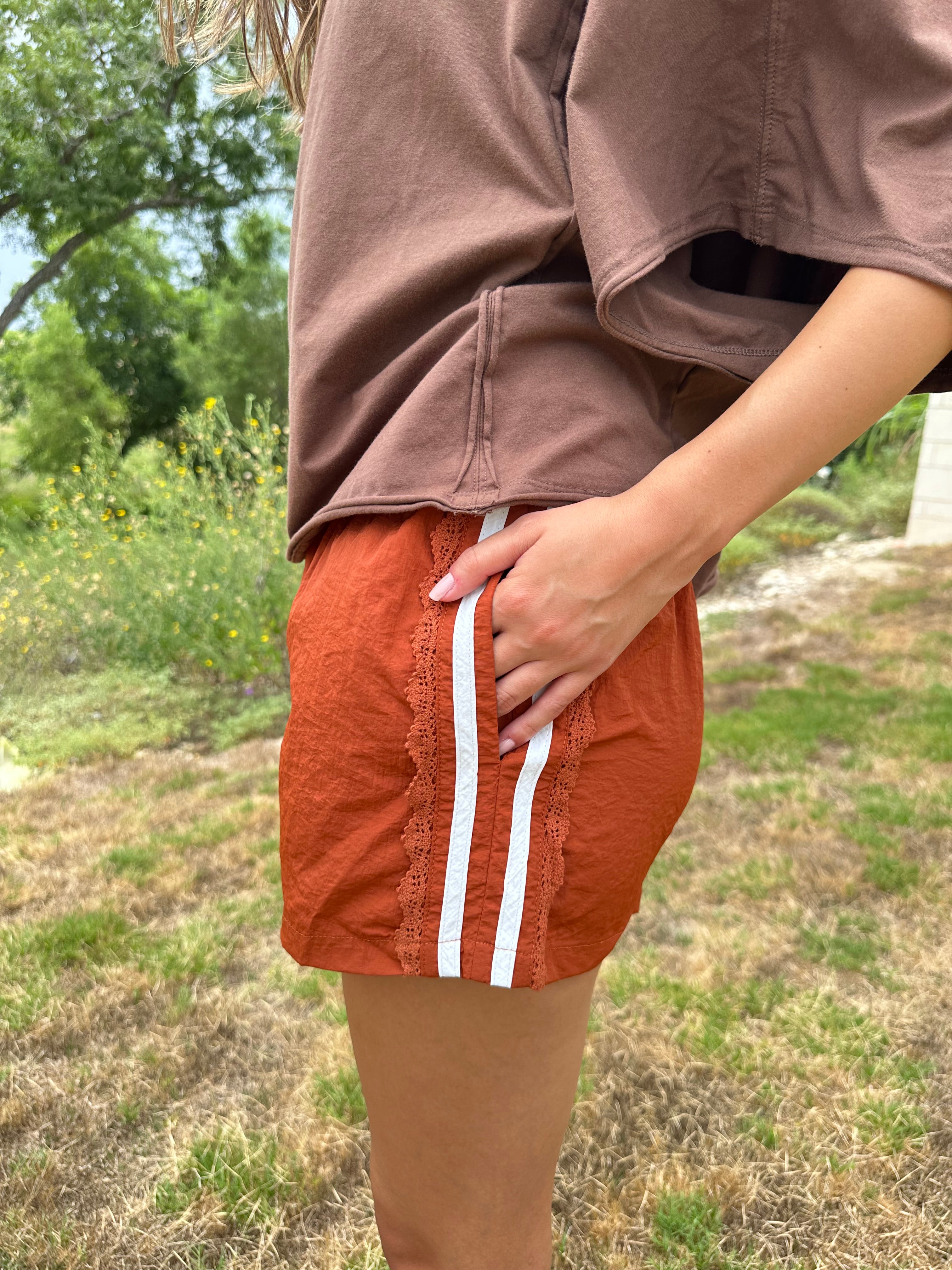 A person outdoors wearing Texas Burnt orange shorts with two white stripes down the side, paired with a brown top. The background shows grass and trees.