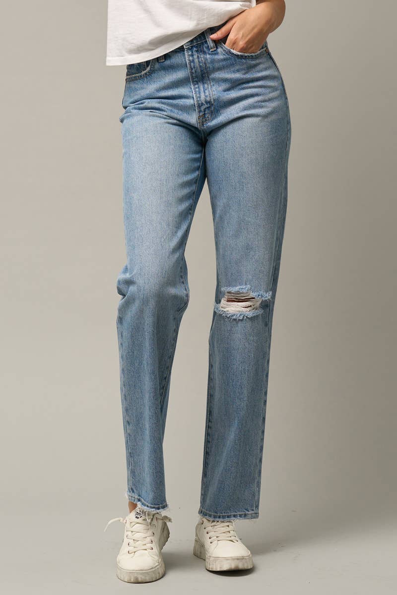 A person wearing light-wash blue distressed jeans with a straight-to-medium leg, paired with a white t-shirt and white sneakers, shown from the waist down against a neutral gray studio background.