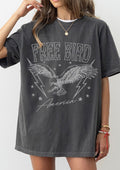 A woman wearing an oversized dark gray washed graphic t-shirt with a distressed white print of an eagle, lightning bolts, stars, and the text 'FREE BIRD America'.