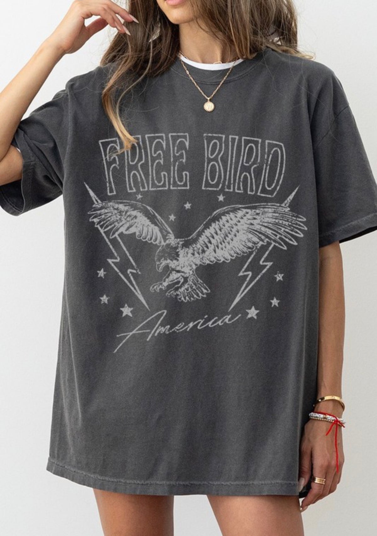A woman wearing an oversized dark gray washed graphic t-shirt with a distressed white print of an eagle, lightning bolts, stars, and the text 'FREE BIRD America'.
