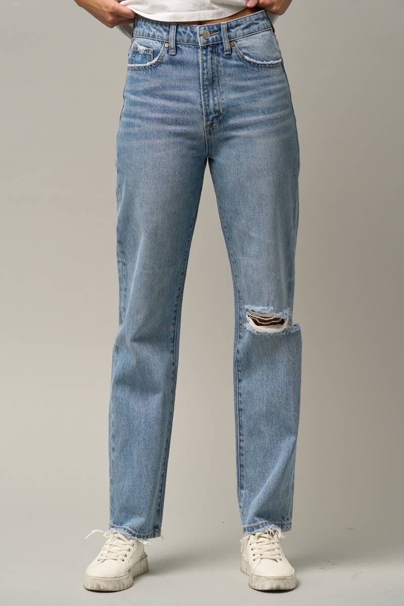 A person wearing light-wash blue distressed jeans with a ripped knee detail, paired with white sneakers, shown from the waist down against a neutral gray studio background.
