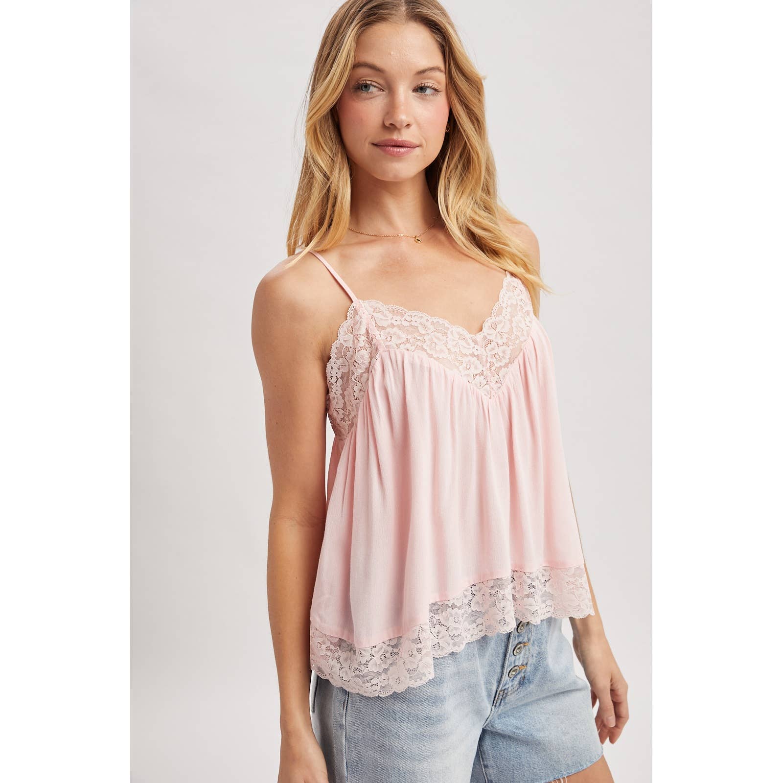 Woman wearing a pink lace-trimmed top against a plain background