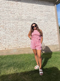 Woman in a red and white checkered dress standing in front of a brick wall.