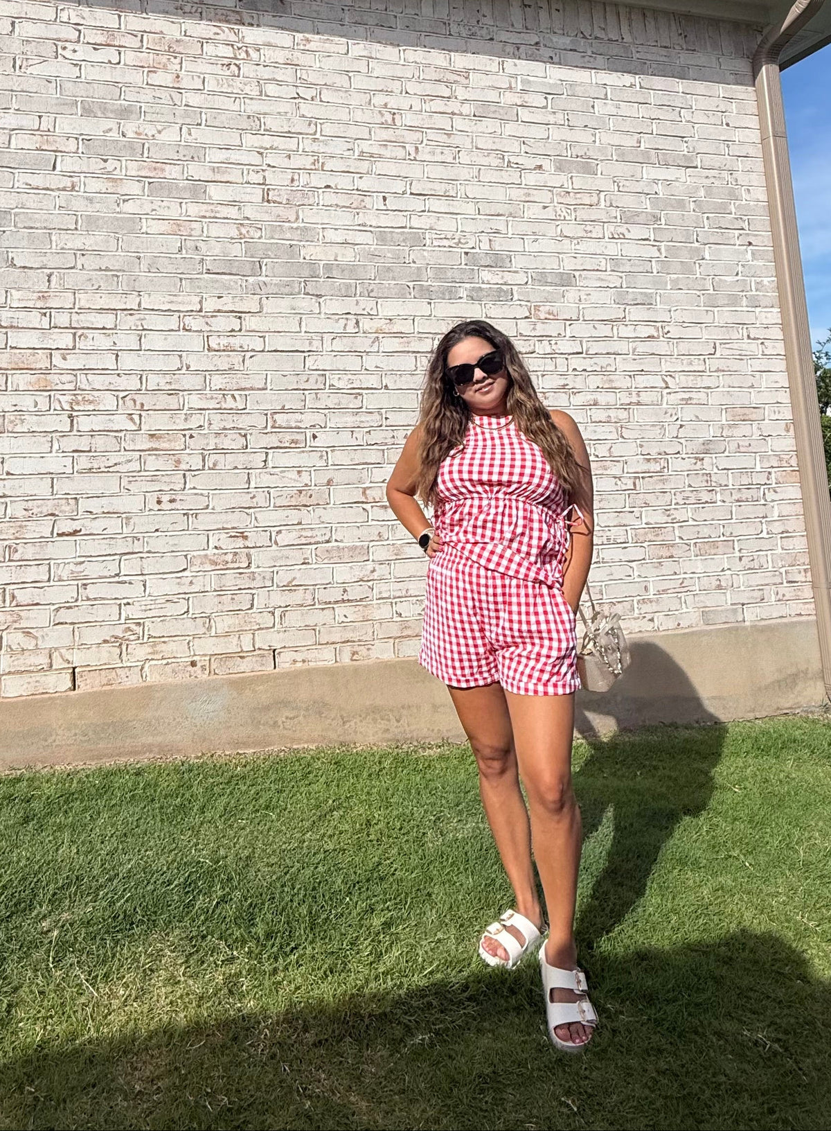 Woman in a red and white checkered dress standing in front of a brick wall.