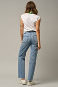 A woman is shown from behind wearing light-wash blue straight-leg jeans, a white sleeveless top, and white sneakers against a neutral gray studio background.