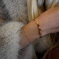 Close-up of a person wearing a gold chain bracelet on a fur surface