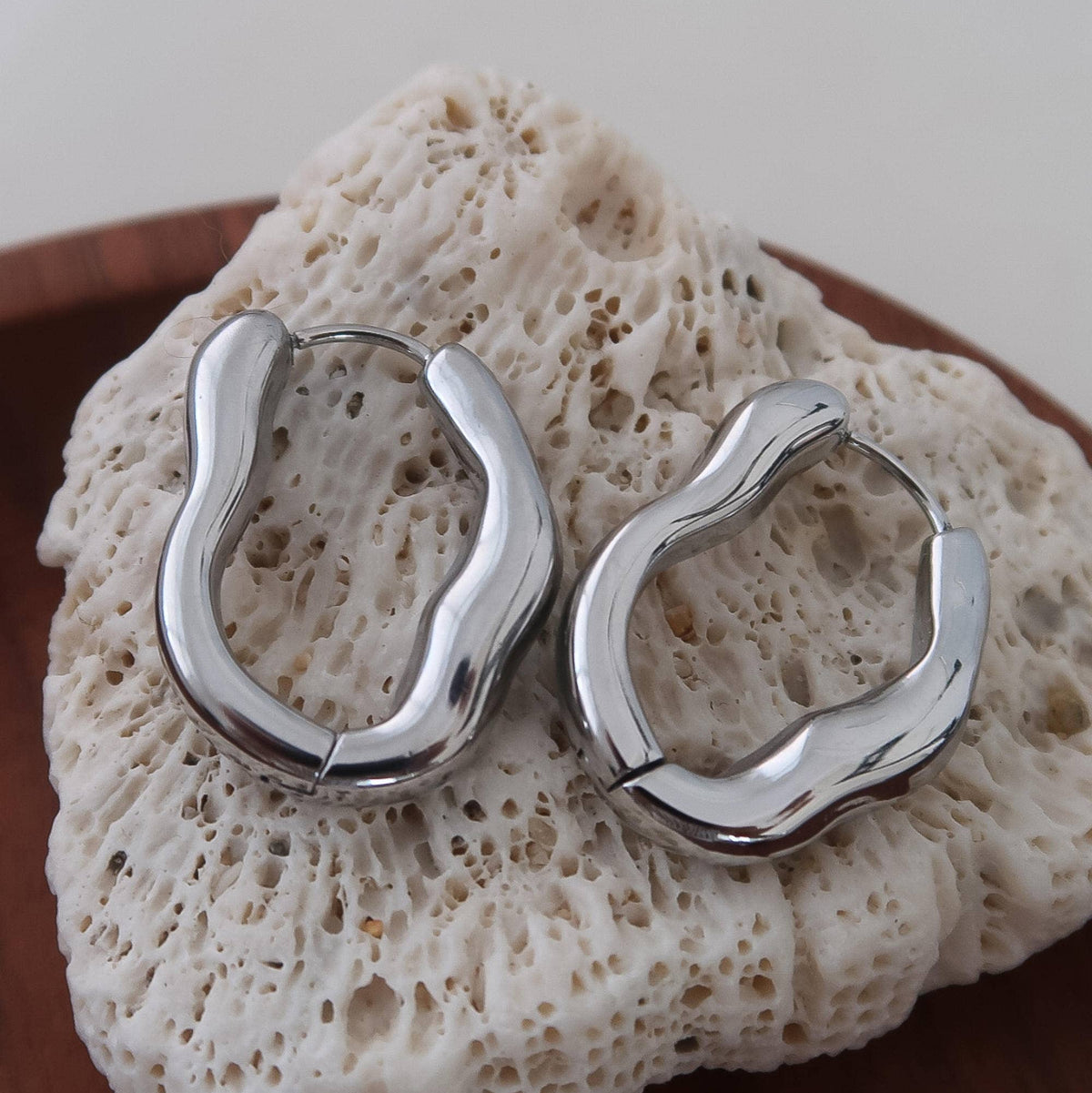Silver, white gold-plated hoop earrings in a chunky, sculpted oval shape. 