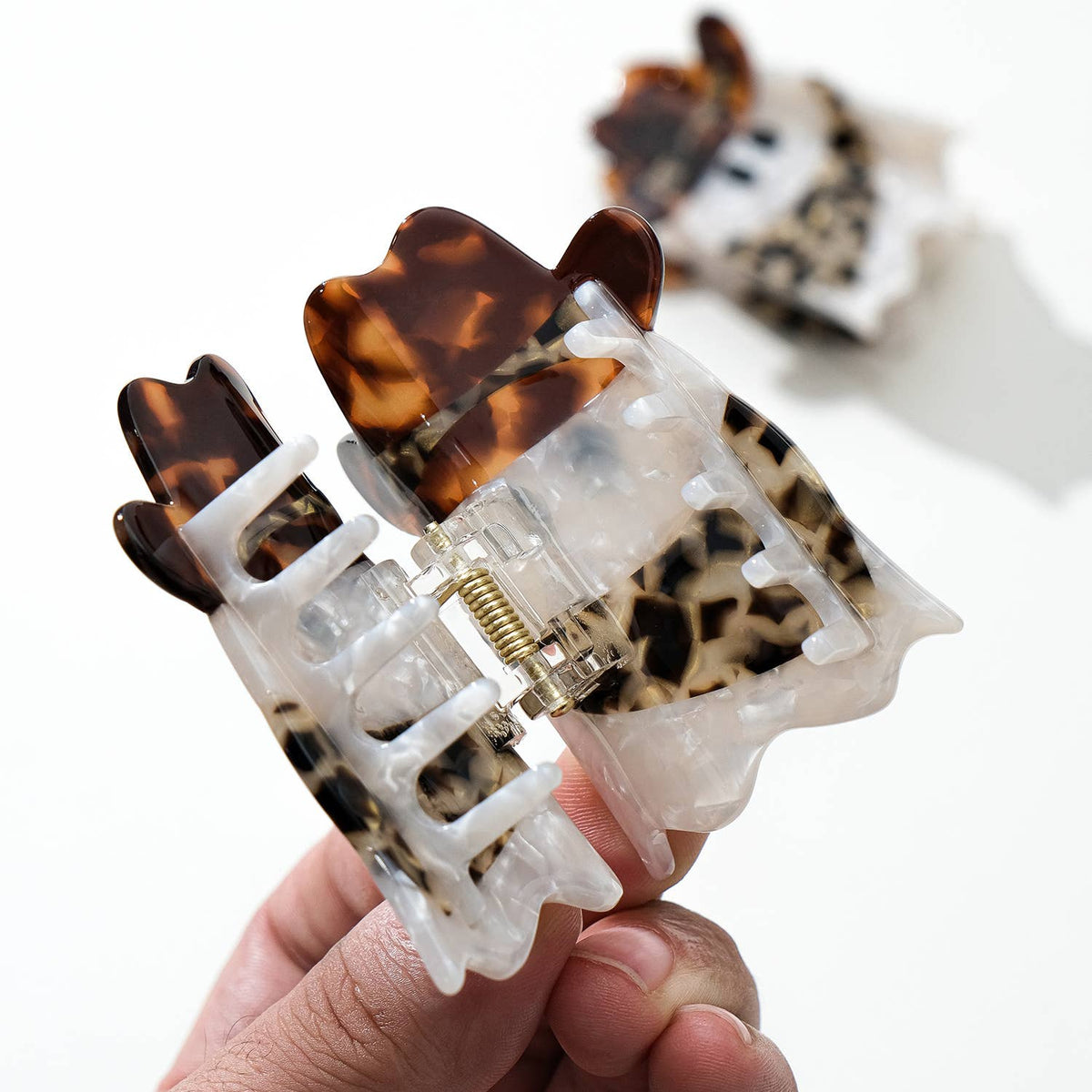 Tortoiseshell and leopard print hair clip held by a hand on a white background
