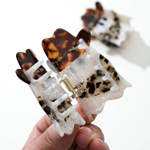 Tortoiseshell and leopard print hair clip held by a hand on a white background