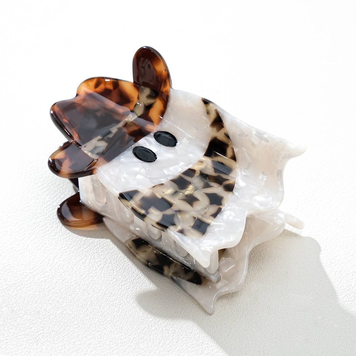 A decorative hair claw clip with a layered design, featuring a translucent white top layer, a black-and-white patterned middle layer, and a classic brown tortoiseshell bottom layer, photographed on a white textured background.