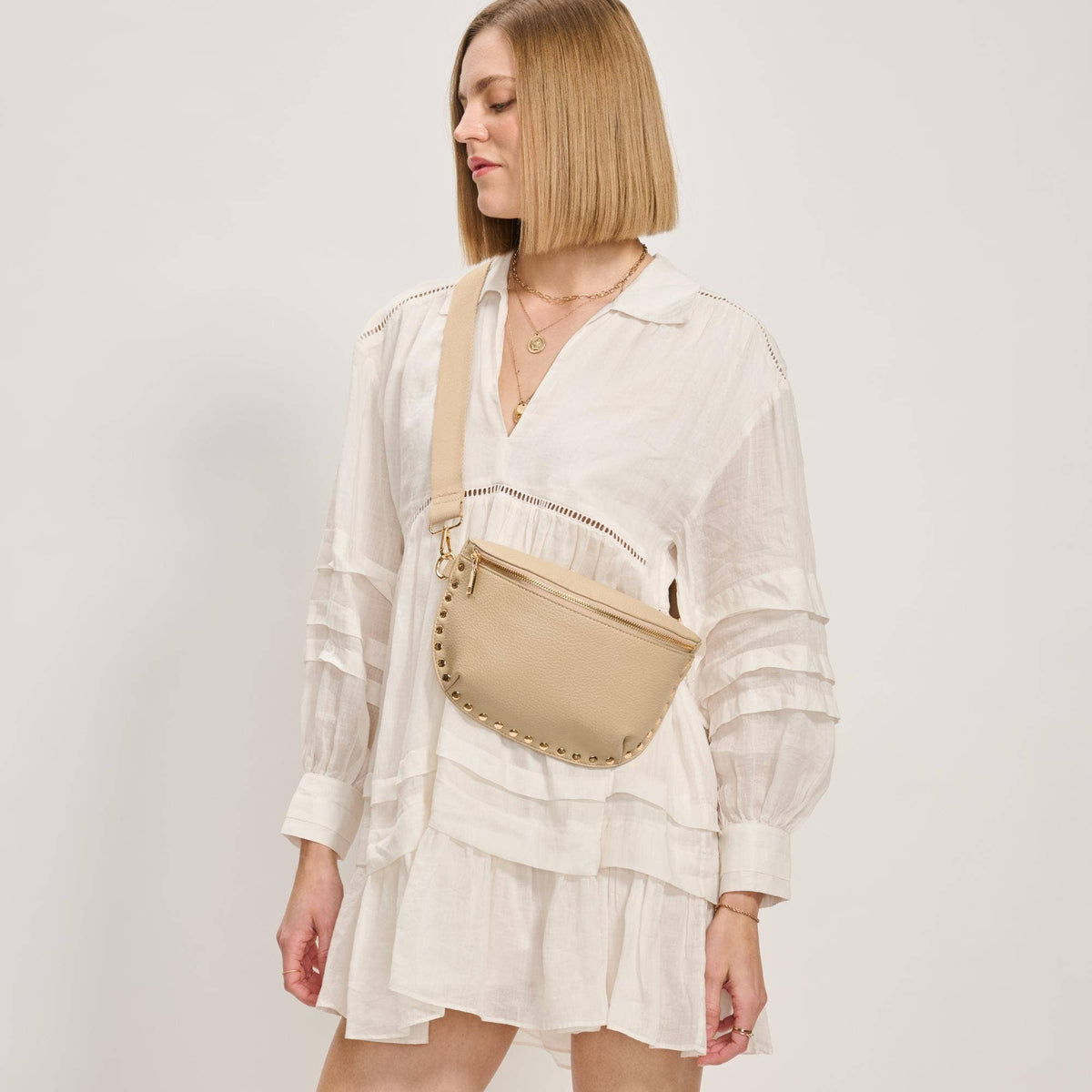 Woman wearing a white dress with a beige crossbody bag on a plain background
