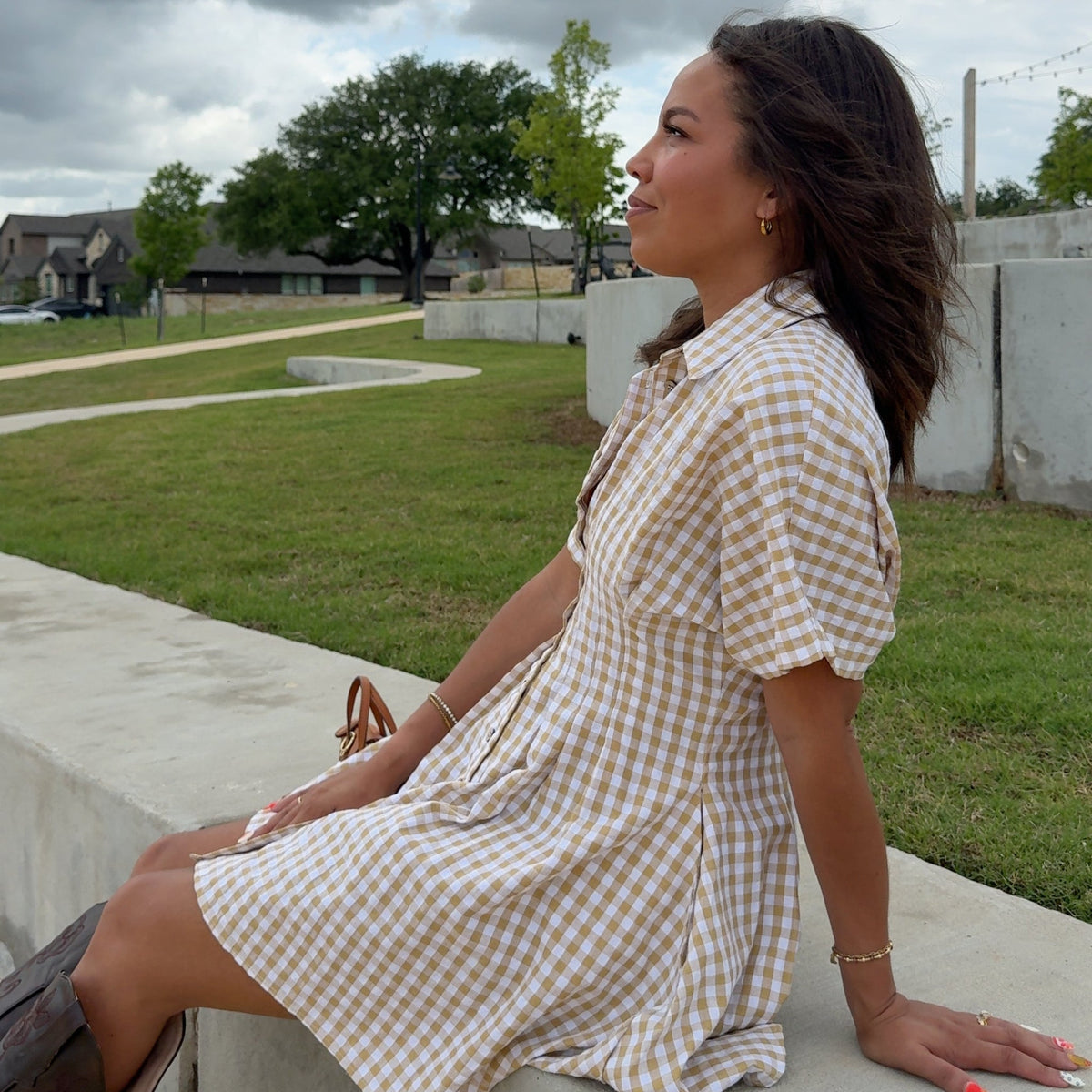 Woman in a checkered dress standing on a grassy area with a cloudy sky.