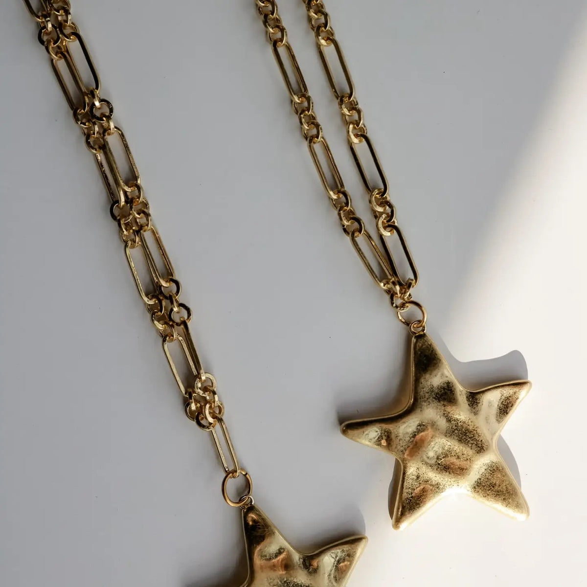 Gold-toned metal necklace with a textured star pendant, photographed on a light gray background with soft shadows.