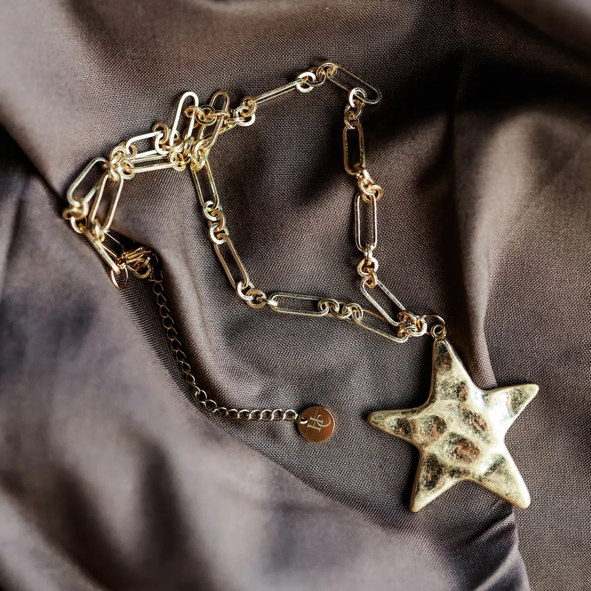 Gold chain necklace with a star pendant on a brown fabric background