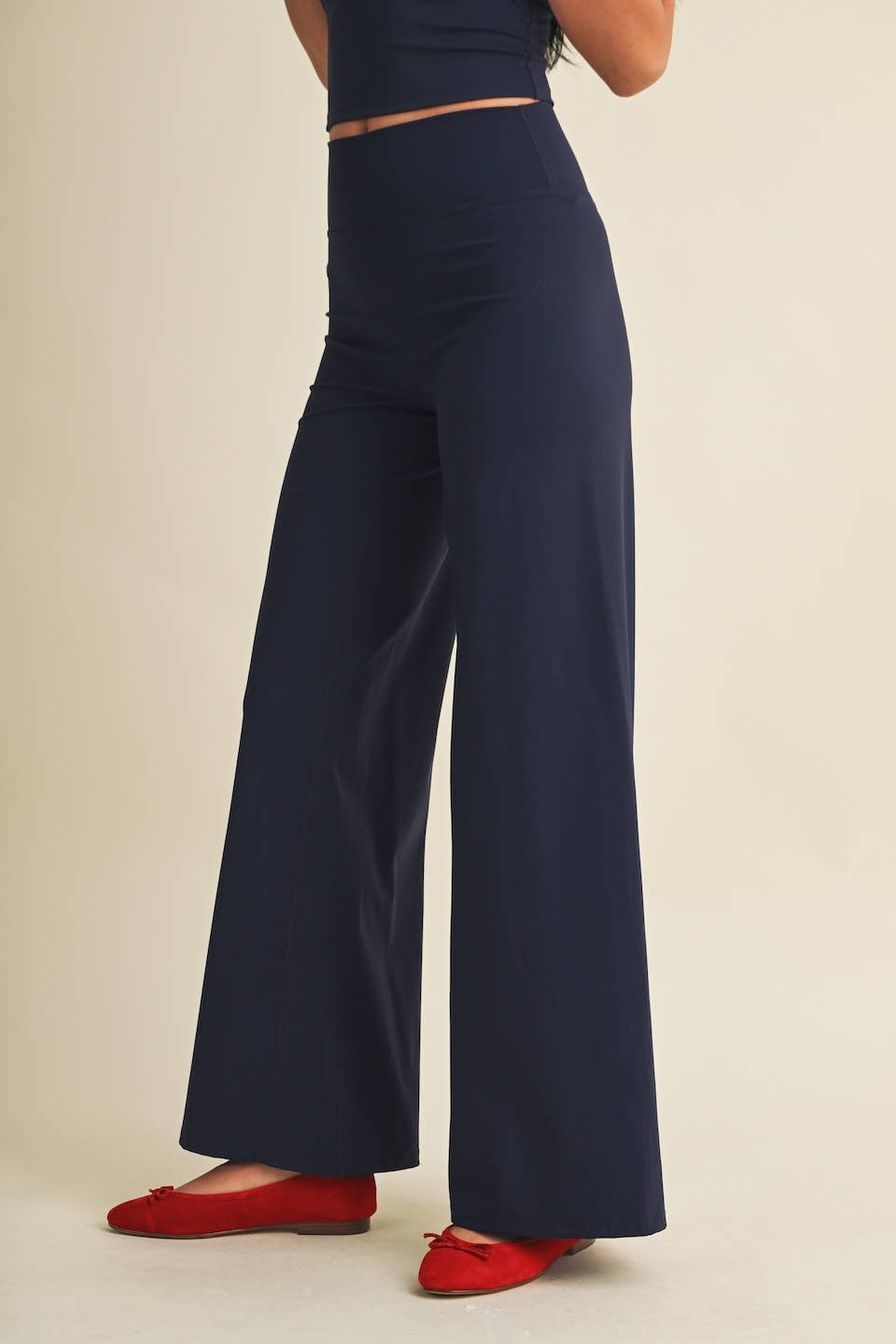 A person wearing high-waisted navy wide-leg pants with a matching navy top, paired with red flats, shown against a plain beige studio background.