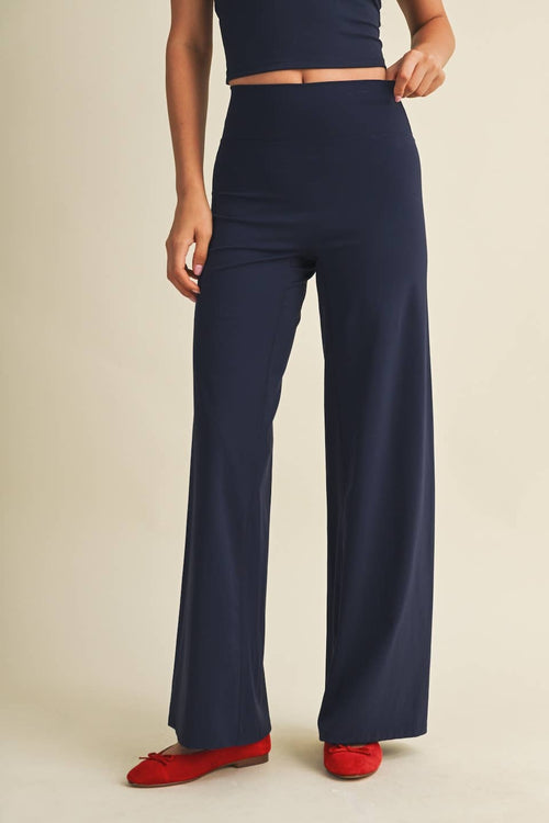 A model wearing navy blue wide-leg trousers and red flats, shown from the waist down against a solid beige background.