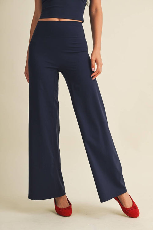 A model wearing navy blue wide-leg pants with a high waist, paired with red flats, shown from the waist down against a solid beige background.