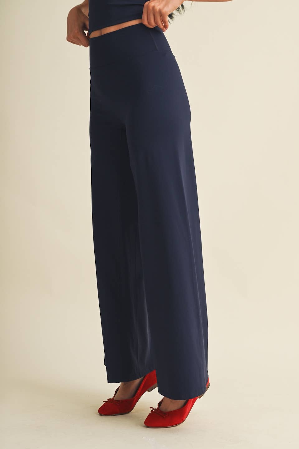 A person wearing navy wide-leg trousers with a matching navy top and red pointed-toe heels, shown from the waist down against a plain light beige studio background.
