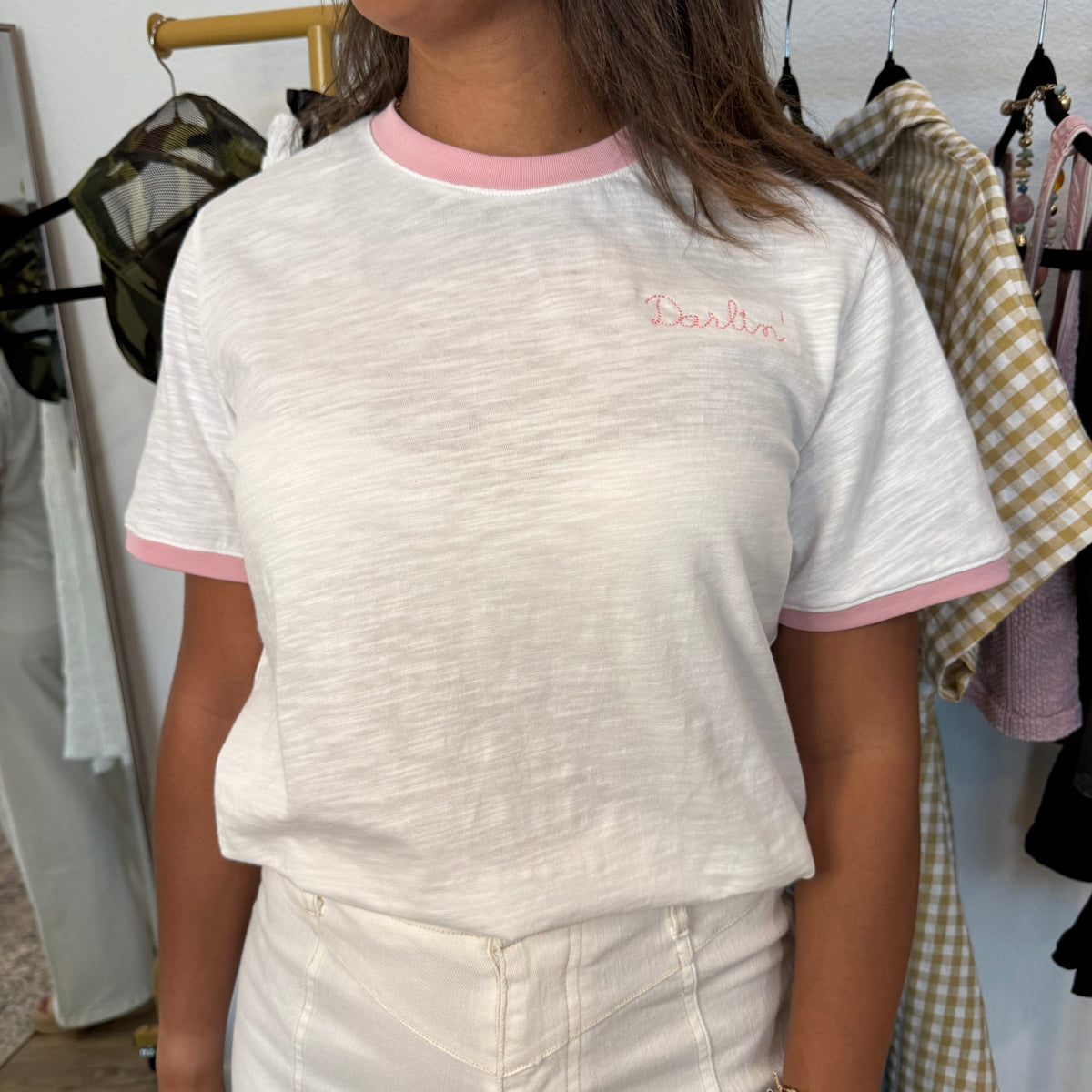 Person wearing a white t-shirt with pink trim and a logo, standing in a clothing store.