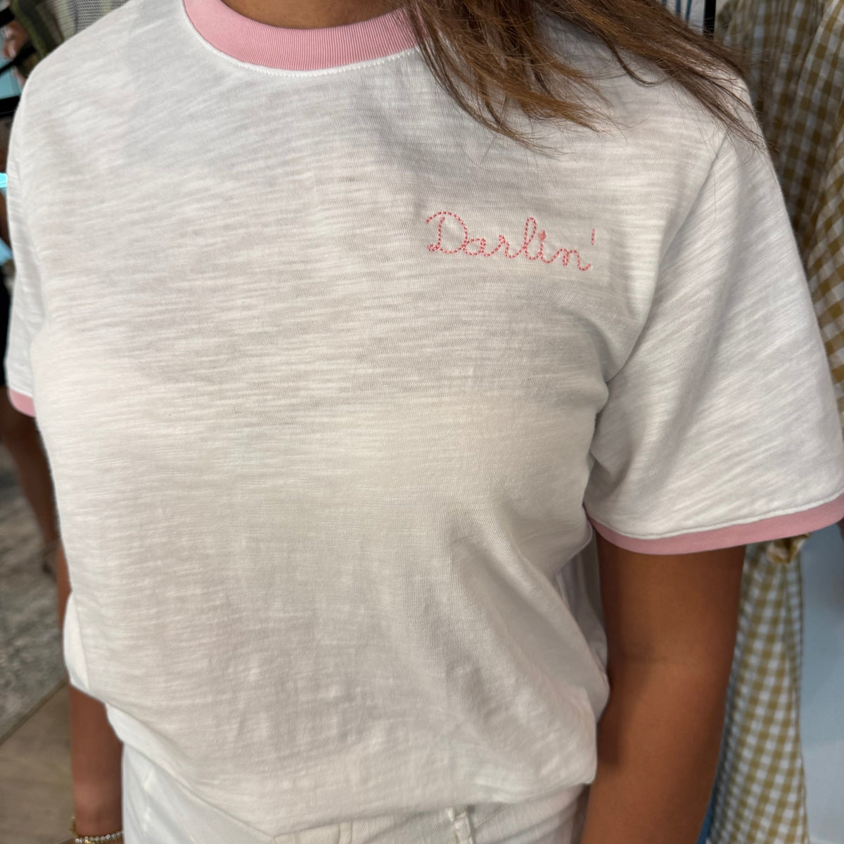 Person wearing a white t-shirt with 'Darlin' embroidered on it, standing indoors.