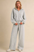 A woman modeling a light gray zip-up hoodie and matching wide-leg sweatpants set against a solid beige studio background.