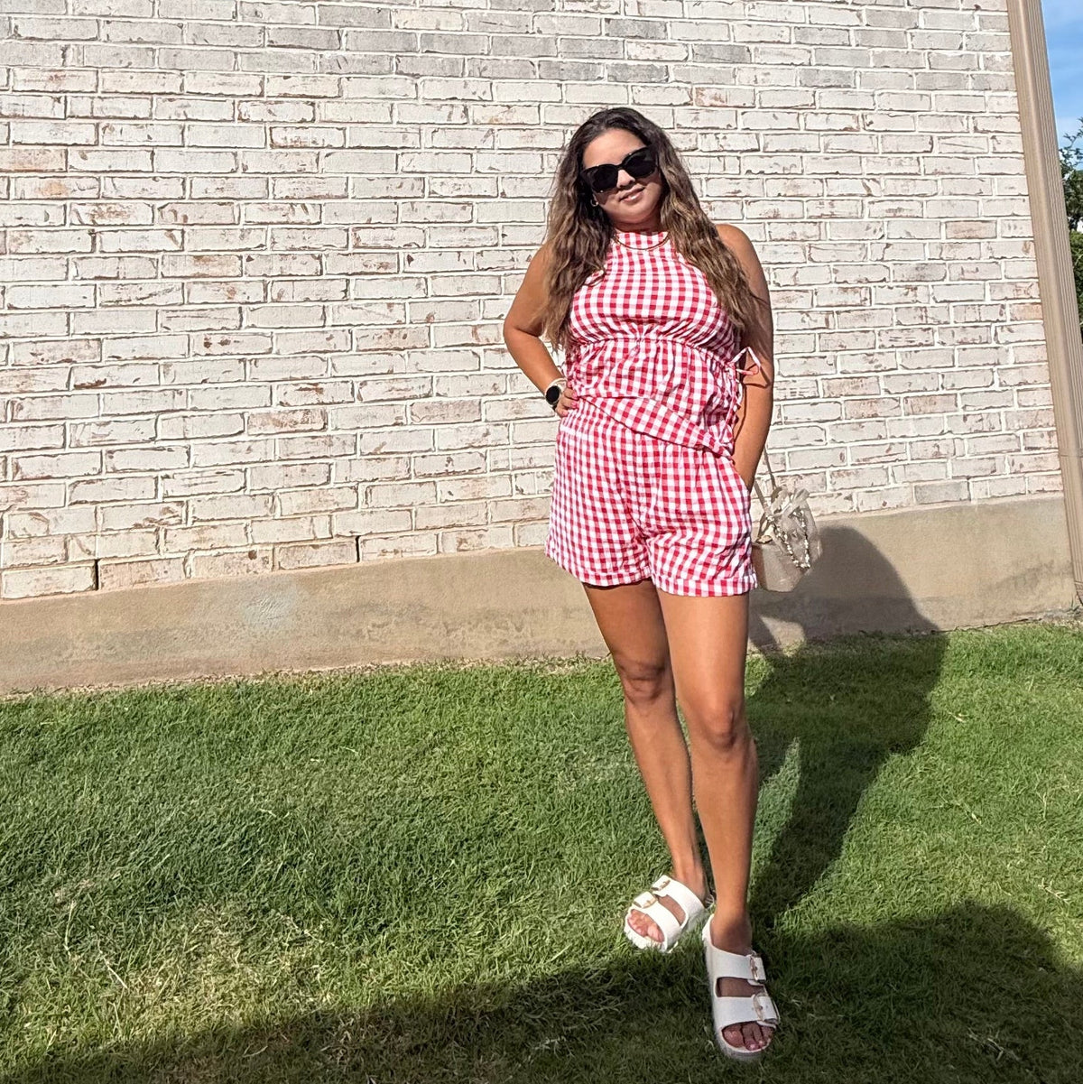 Woman in a red and white checkered dress standing in front of a brick wall.
