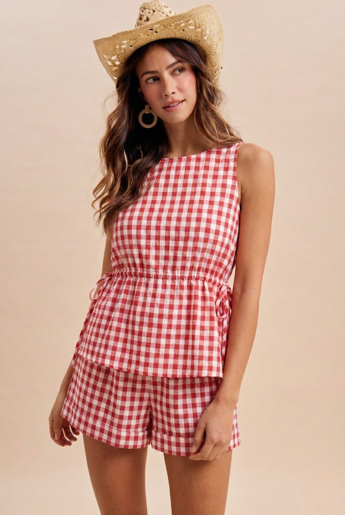 Woman wearing a red and white checkered outfit with a straw hat on a beige background