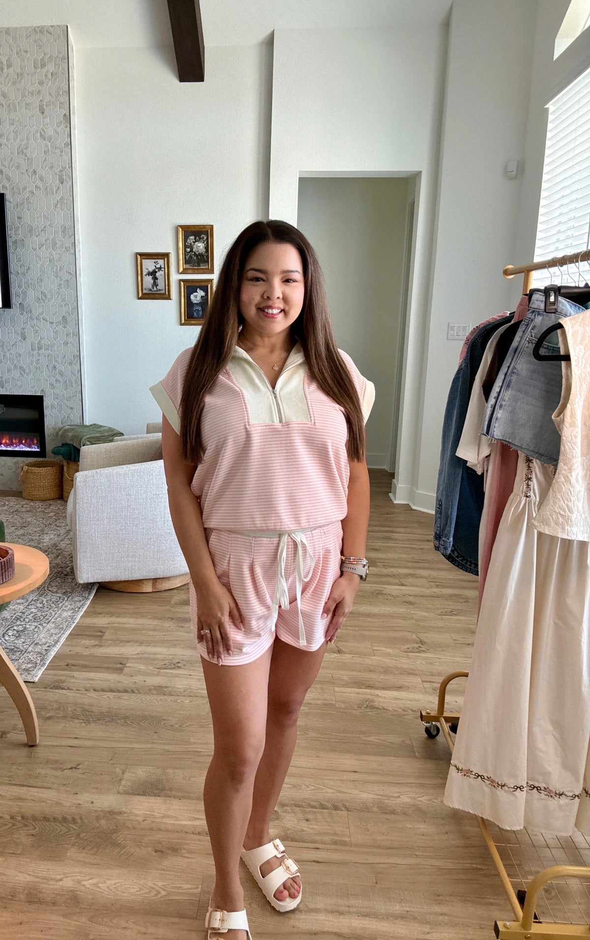 Woman in a pink outfit standing in a room with wooden flooring and a clothing rack.