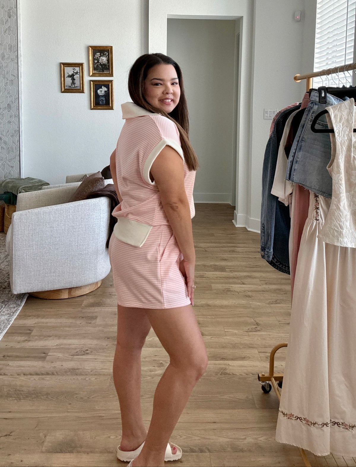 Woman in a pink two piece set standing in a room with clothing racks and a fireplace.