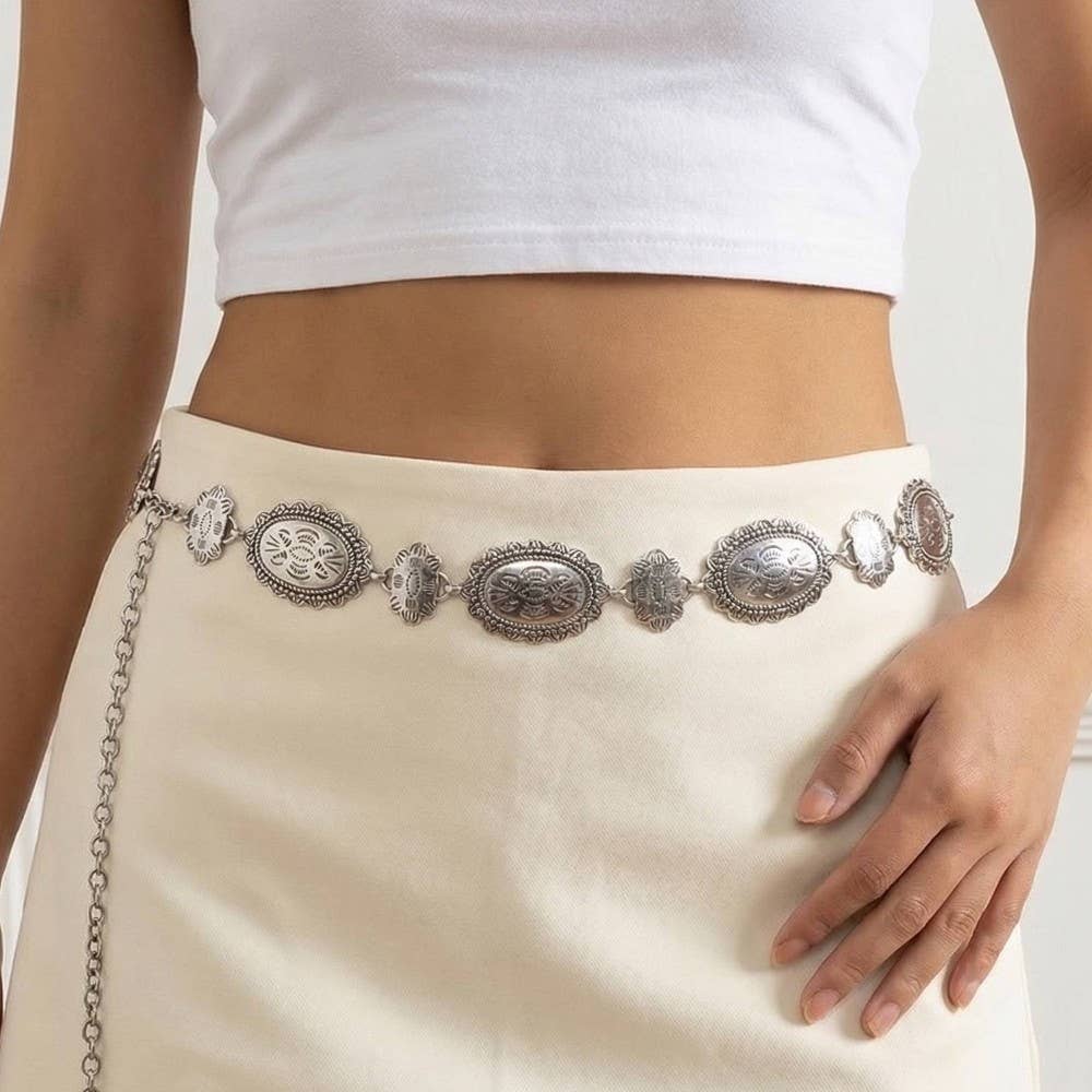 Decorative silver belt with chain detail worn by a person in a white top and beige skirt.