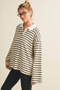 A woman wearing a cream and black horizontally striped long-sleeve polo shirt with a white collar, paired with black pants, against a plain beige background.