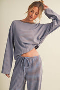 A woman modeling a matching two-piece loungewear set with a long-sleeve cropped top and drawstring pants, featuring a blue and beige horizontal stripe pattern against a solid light beige background.