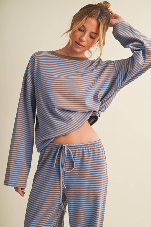 A woman modeling a matching two-piece loungewear set with a long-sleeve cropped top and drawstring pants, featuring a blue and beige horizontal stripe pattern against a solid light beige background.