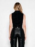 A woman shown from the back wearing a black sleeveless velvet vest and black leather fringe pants against a plain white studio background.