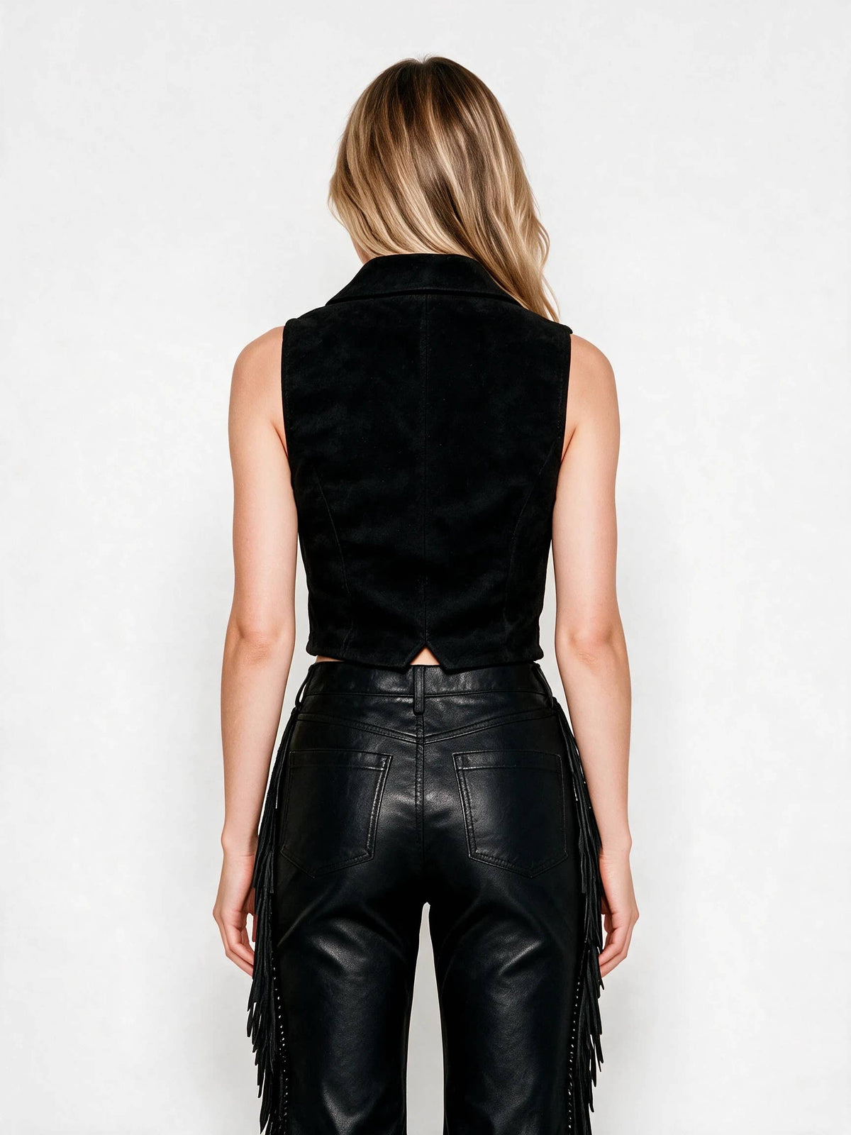 A woman shown from the back wearing a black sleeveless velvet vest and black leather fringe pants against a plain white studio background.